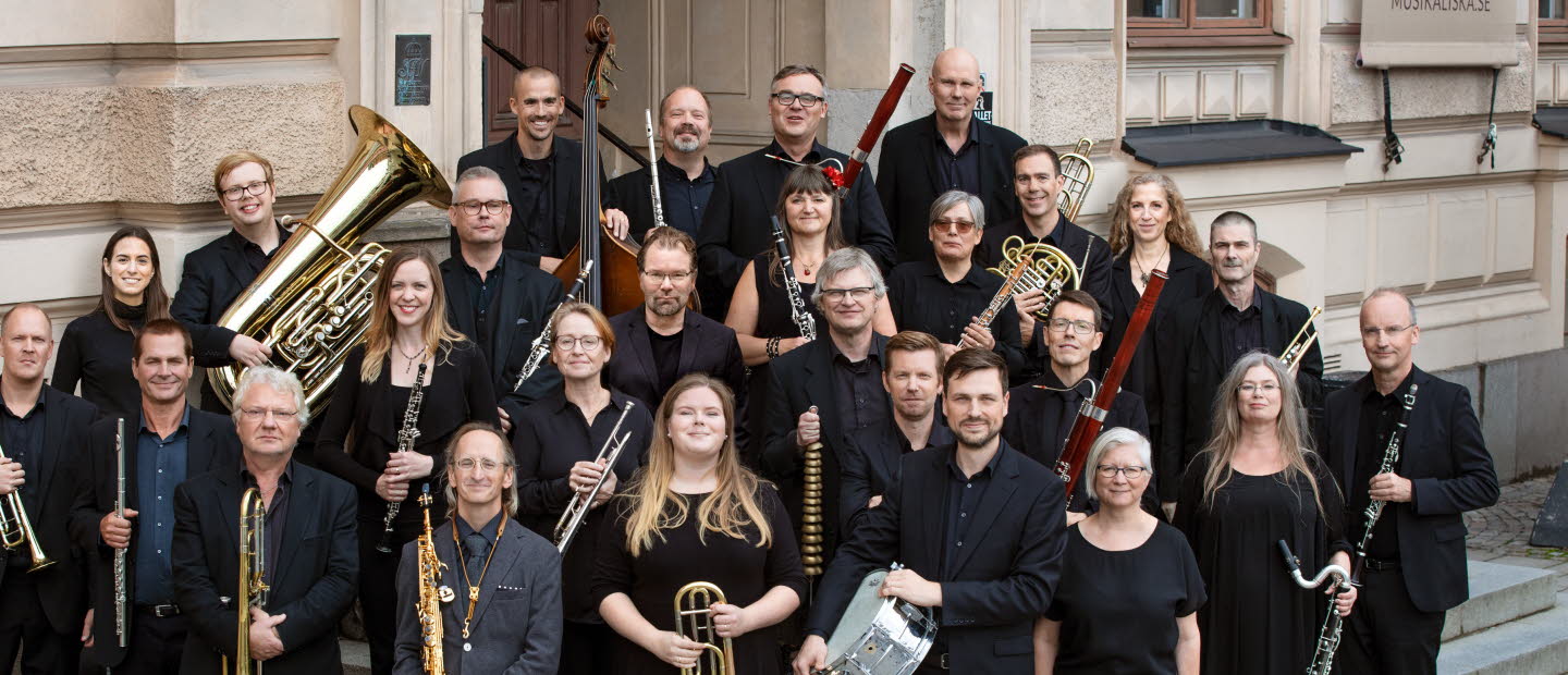 Symfoniorkester står på en trappa, ett tjugotal musiker som håller sina instrument i sina händer.