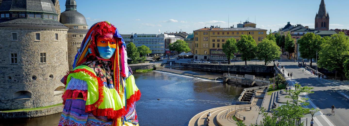 Skulptur av en färgglad kvinna, i bakgrunden syns Örebro slott och ån.
