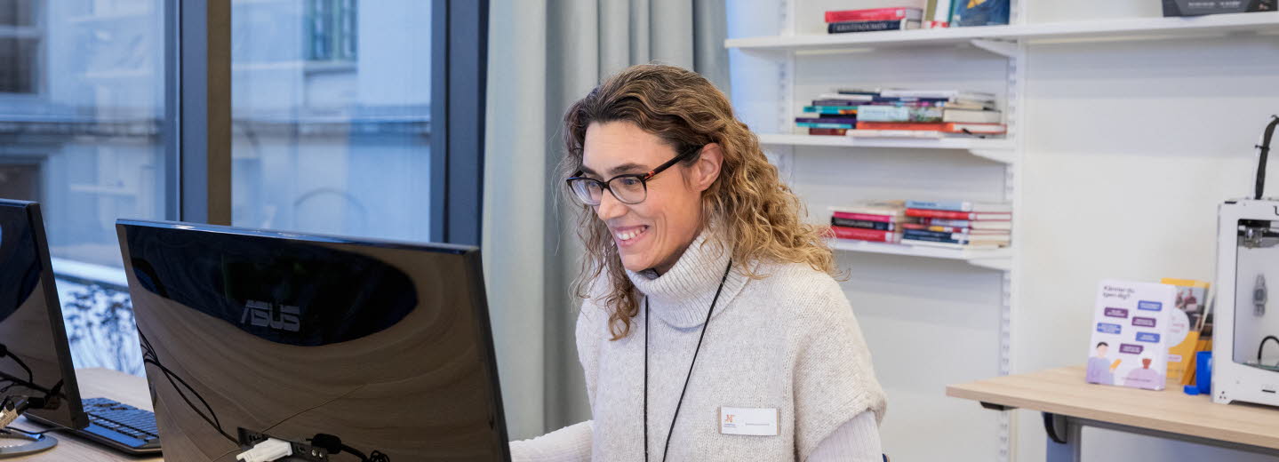 Kvinnlig bibliotekarie sitter framför datorn och tar del samtal som pågår på skärmen.