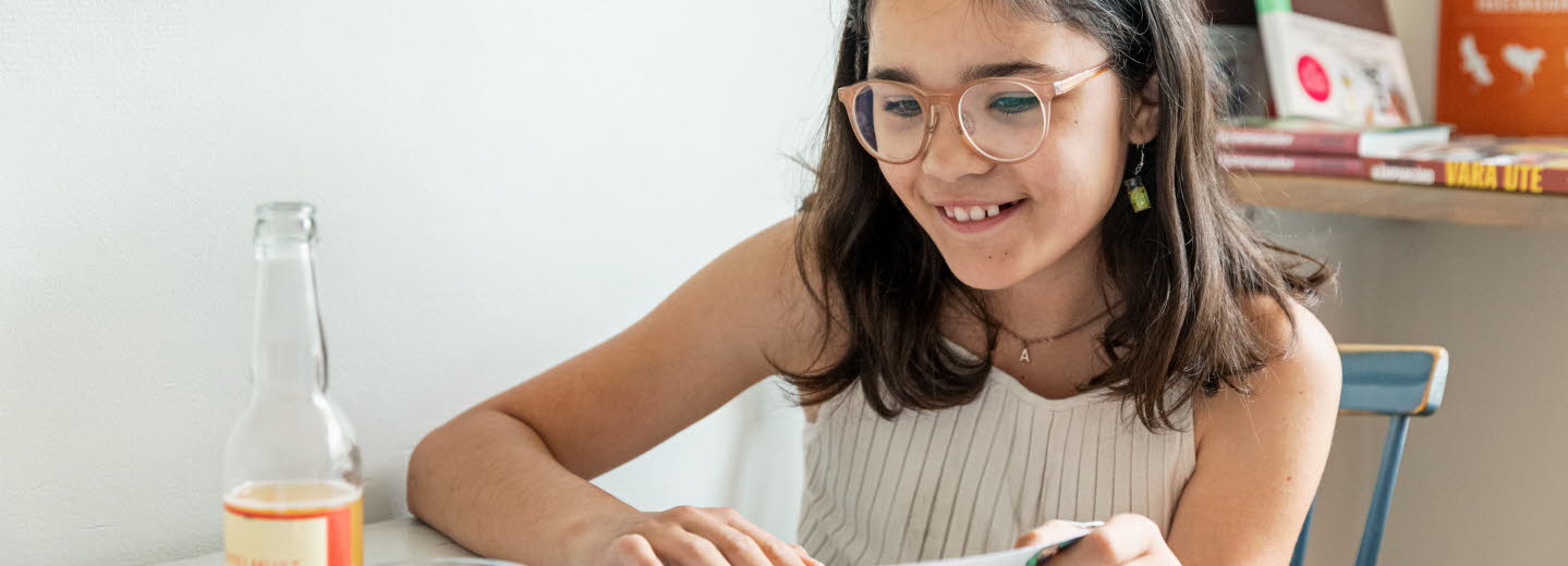 Flicka läser bok vid köksbordet