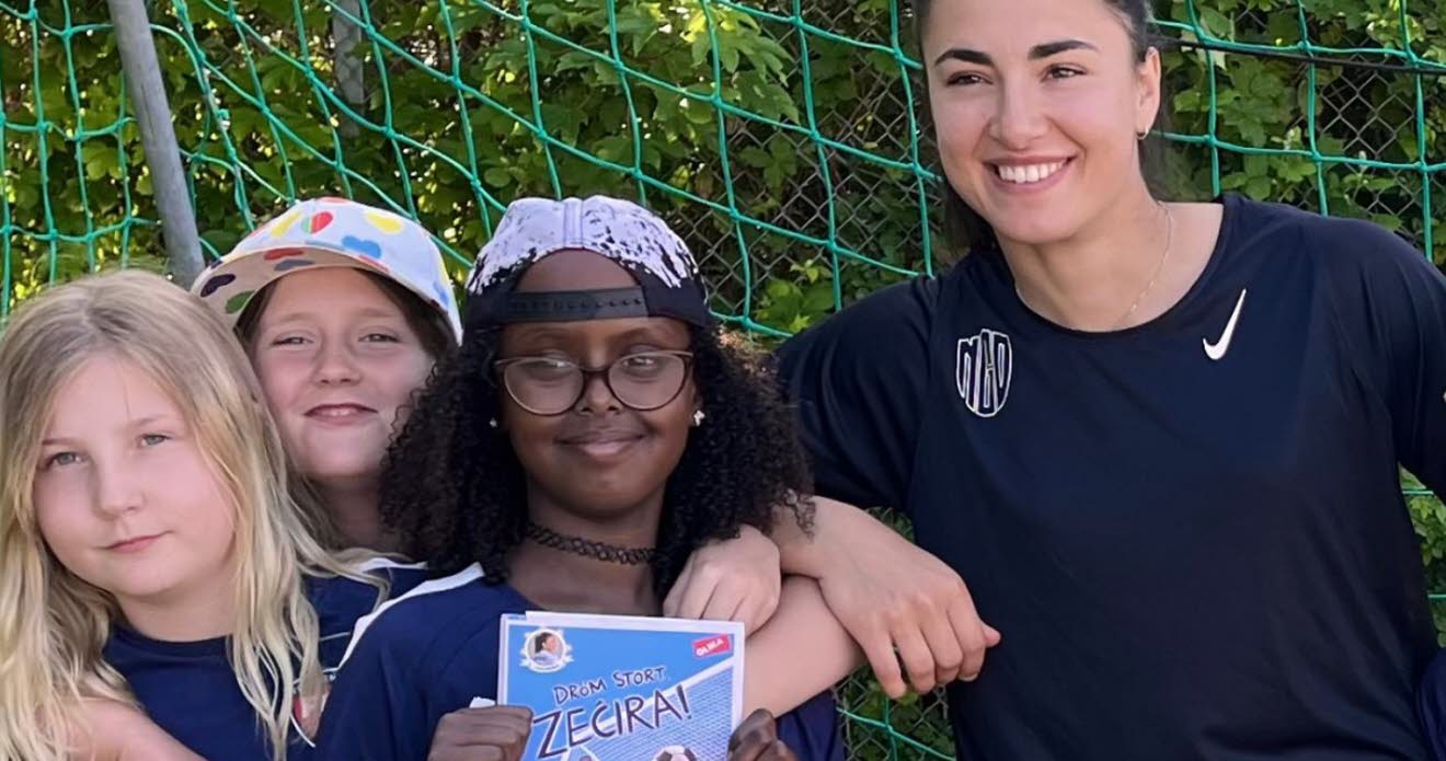 Barn i fotbollskläder som poserar tillsammans med en kvinna i ett fotbollsmål.