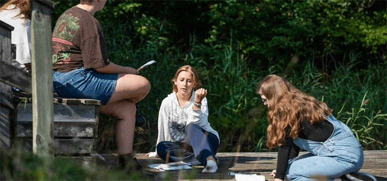 Ungdomar med böcker som sitter och pratar på ett trädäck.