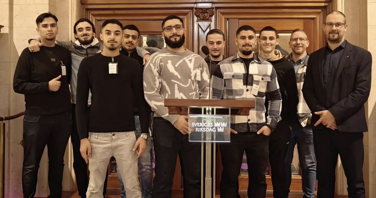 Bild på en grupp mestadels unga män bakom en talarstol som visar att de är i Riksdagen.