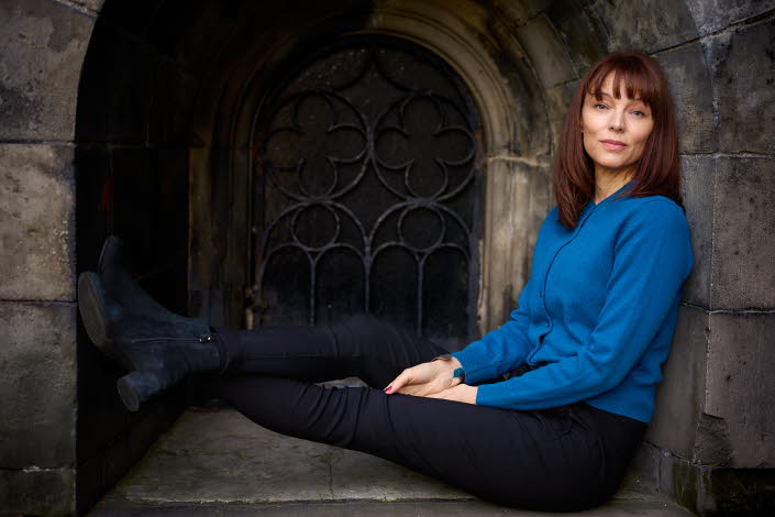 Lina Wolff sits in a window with her legs up, she is looking into the camera and wearing a blue shirt.