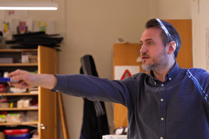 Manlig lärare pekar med en penna i ett klassrum.