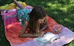 Flicka ligger på en filt i gräset och läser en bok