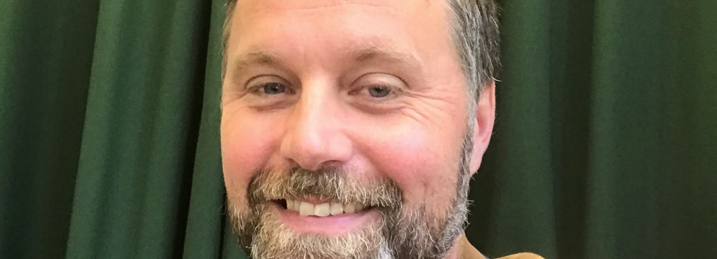 Bild på John Bjerkert, med grön bakgrund.