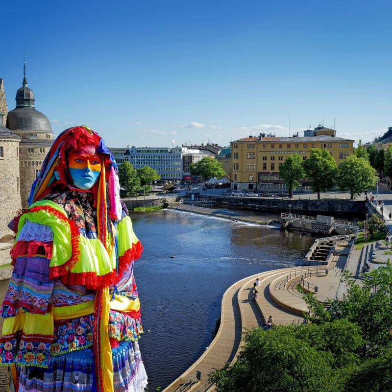 Skulptur av en färgglad kvinna, i bakgrunden syns Örebro slott och ån.