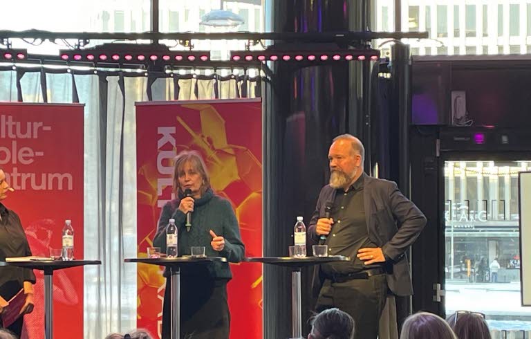 En man och en kvinna på en scen med ståbord och röd bakgrund