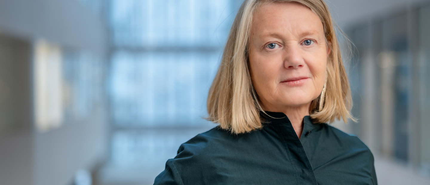 Medelålderskvinna i halvfigur. Blond page och mörkblå blus. 