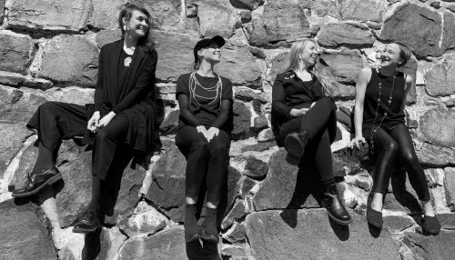 Fyra kvinnor i svartvitt sitter på en stenmur.