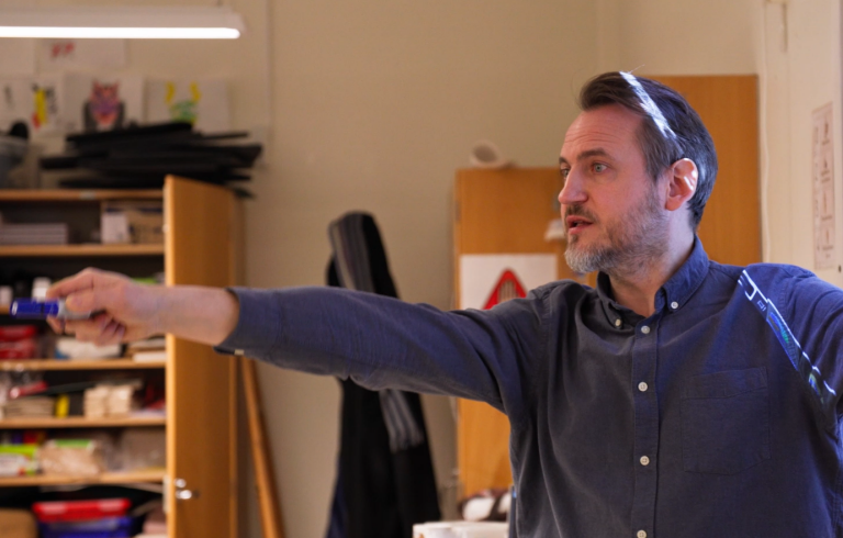 Manlig lärare pekar med en penna i ett klassrum.