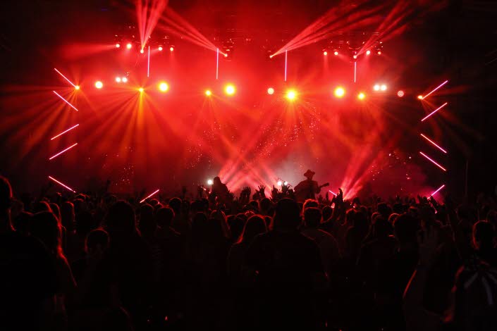 Konsertscen upplyst i rött ljus med publikhav framför.