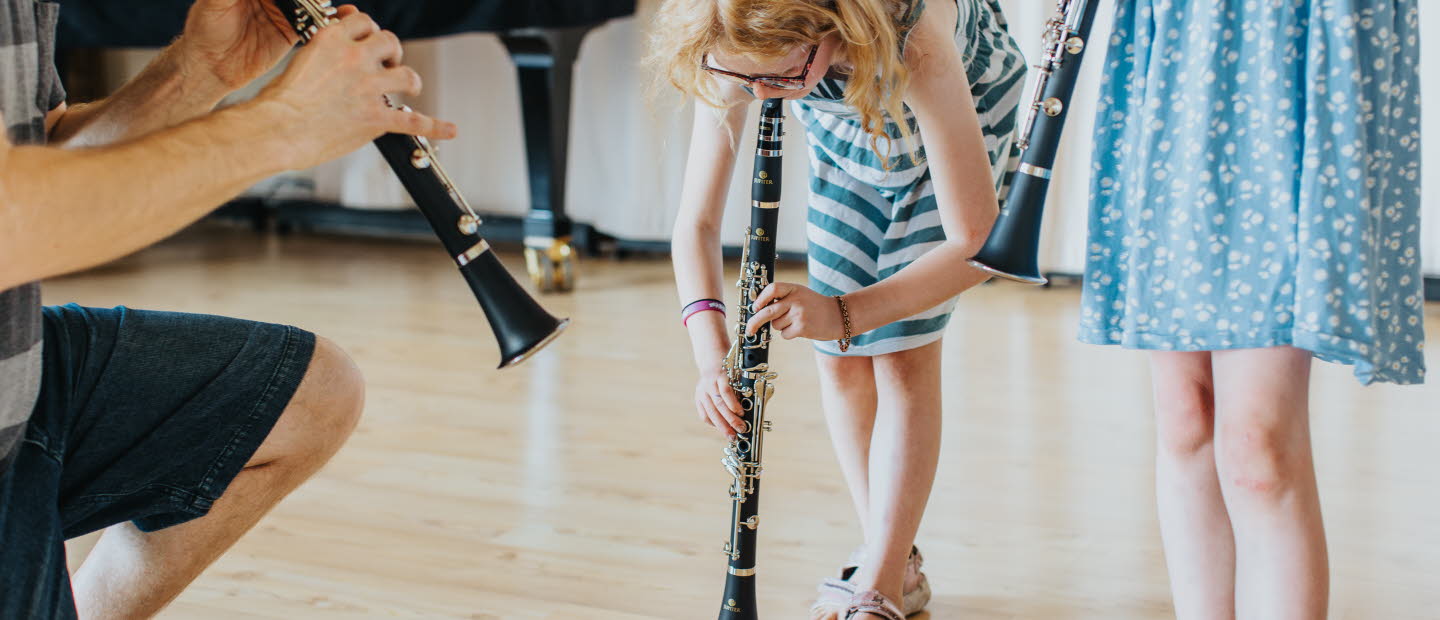 Barn spelar blåsinstrument tillsammans med en vuxen.