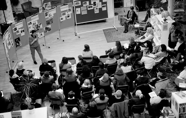  Föreläsning om Women Making HERstory föreläsningssal. Ett 30-tal människor lyssnar till en som står och pratar. Bilden är tagen uppifrån och man ser ingens ansikte tydligt.