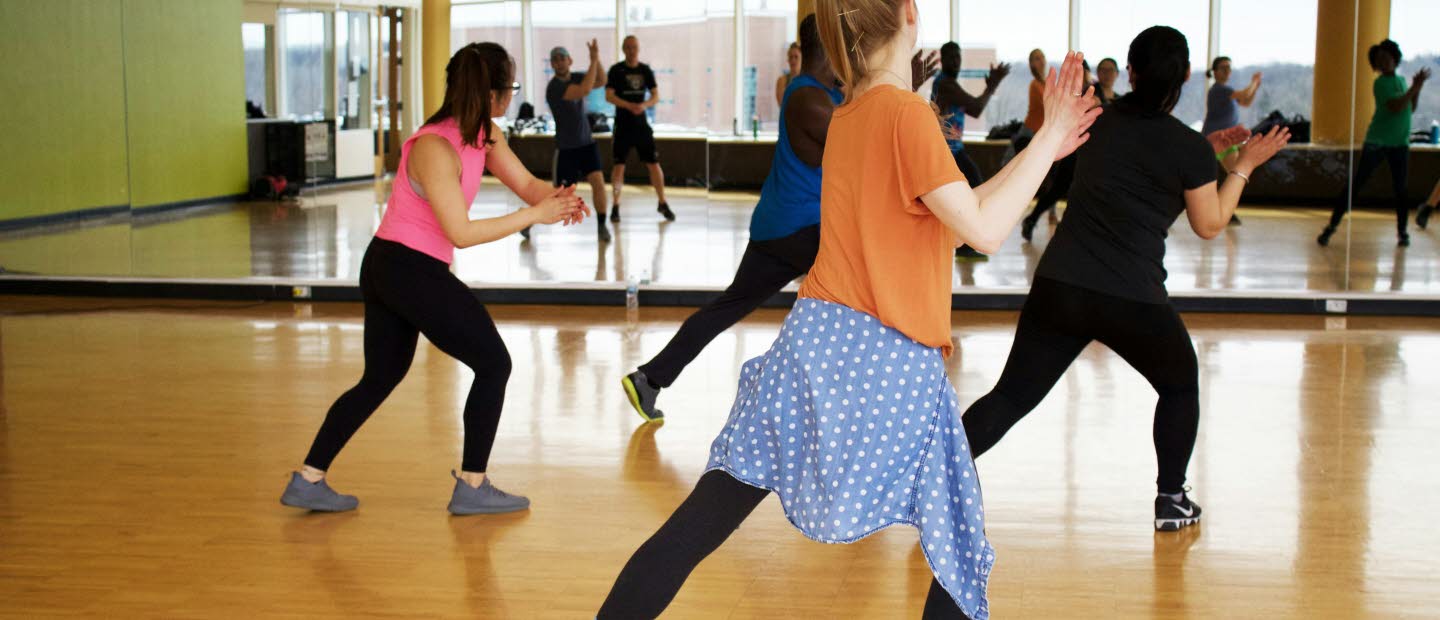 Ungdomar framför stor väggspegel i träningslokal där de tränar dansrörelser. 