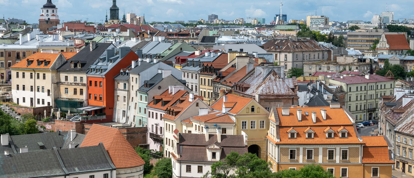 Bild över flera hustak i staden Lublin. I bakgrunden skymtas ett kyrktorn. Vädret är sol med växlande molnighet.