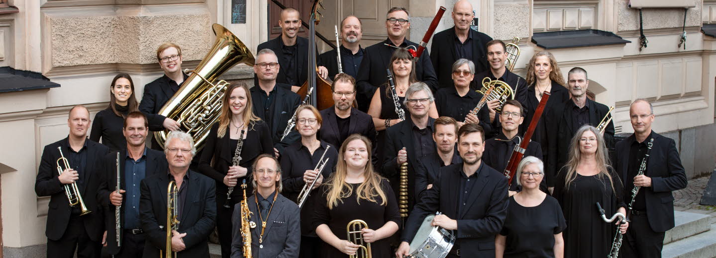 Symfoniorkester står på en trappa, ett tjugotal musiker som håller sina instrument i sina händer.