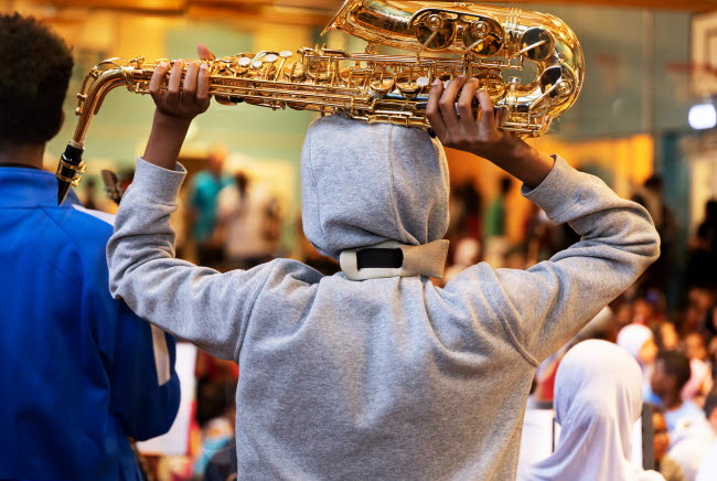 Pojke står i folkvimmel med en saxofon ovanför sitt huvud.