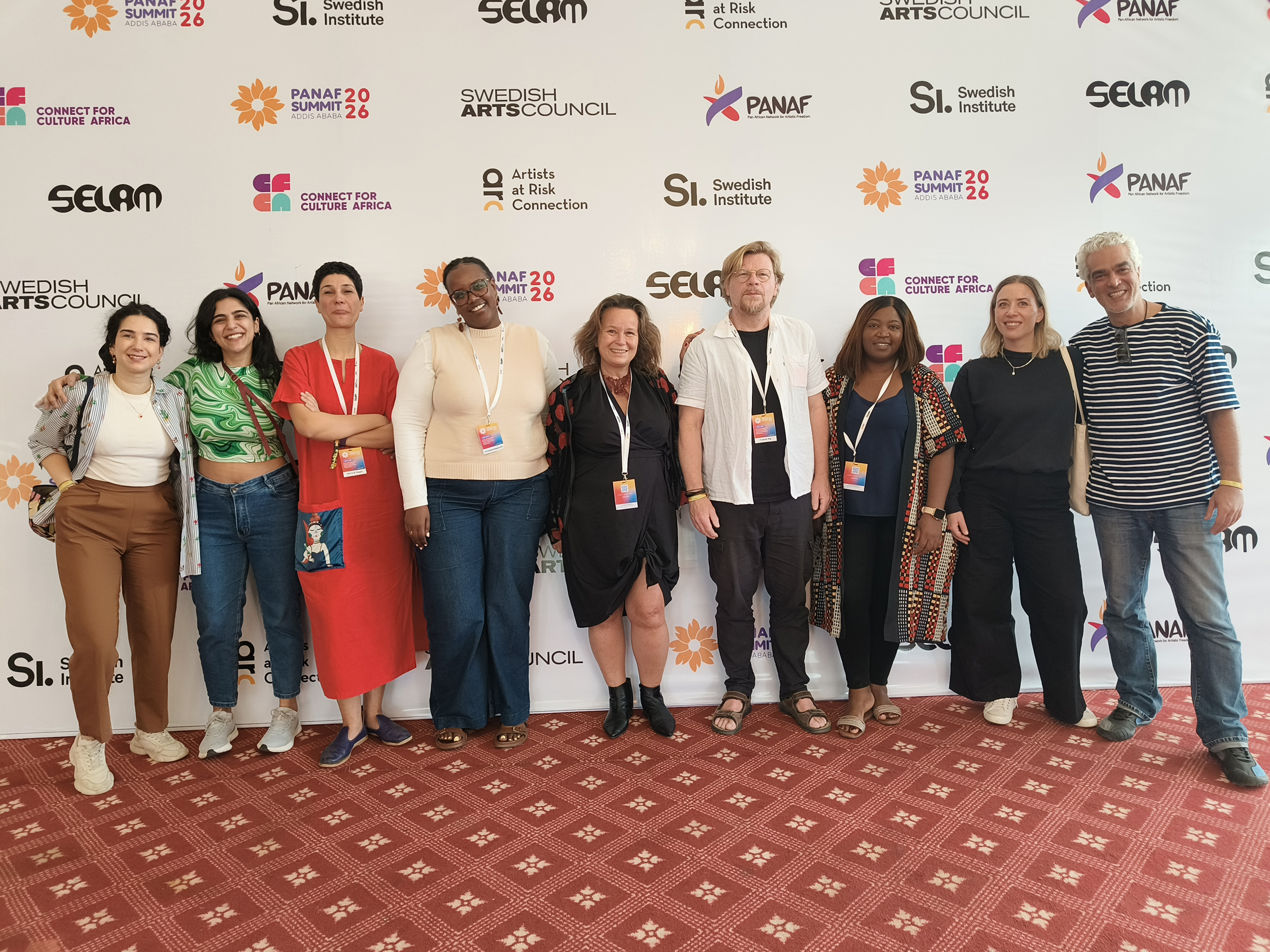 Gruppbild, i bakgrunden syns en v&auml;gg med loggor med medfinansi&auml;rer. Foto: Selam.