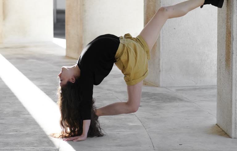 Akrobatisk dansrörelse av Marina Cherry med foten mot en betongpelare.