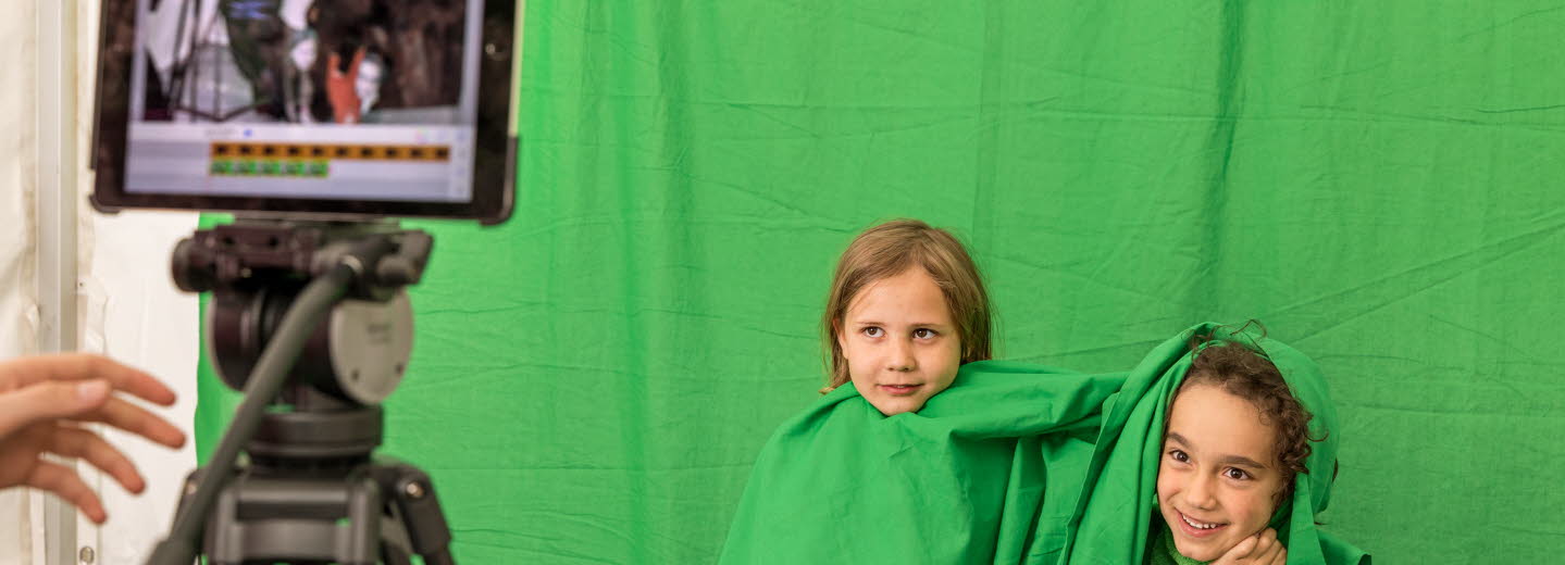 Två barn med gröna kläder blir filmade mot en grön vägg.