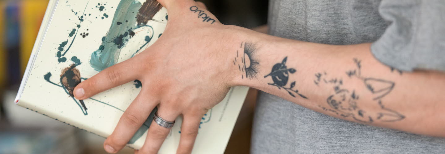 Tatuerade armar som håller i en bok.
