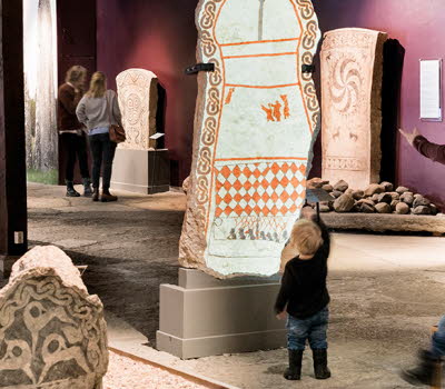 Familj tittar på gotländska bildstenar på Gotlands museum. 