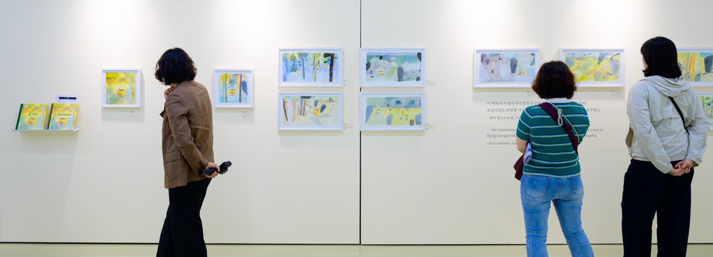 Tre personer tittar på en utställning med teckningar av Eva Lindström under Jeonju internationella bilderboksmässa 2025. Three people are viewing an exhibition of drawings by Eva Lindström at the Jeonju International Picture Book Fair 2025.