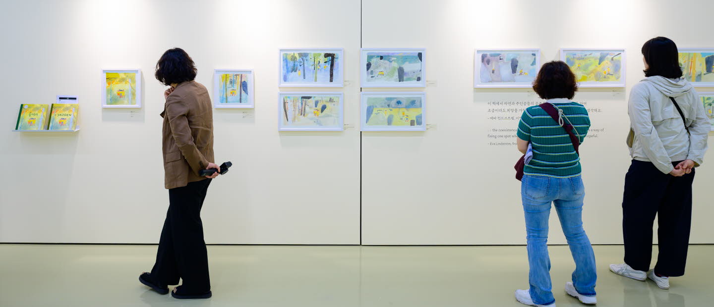 Tre personer tittar på en utställning med teckningar av Eva Lindström under Jeonju internationella bilderboksmässa 2025. Three people are viewing an exhibition of drawings by Eva Lindström at the Jeonju International Picture Book Fair 2025.