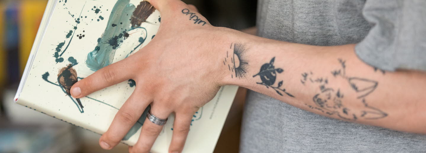 Tatuerade armar som håller i en bok.