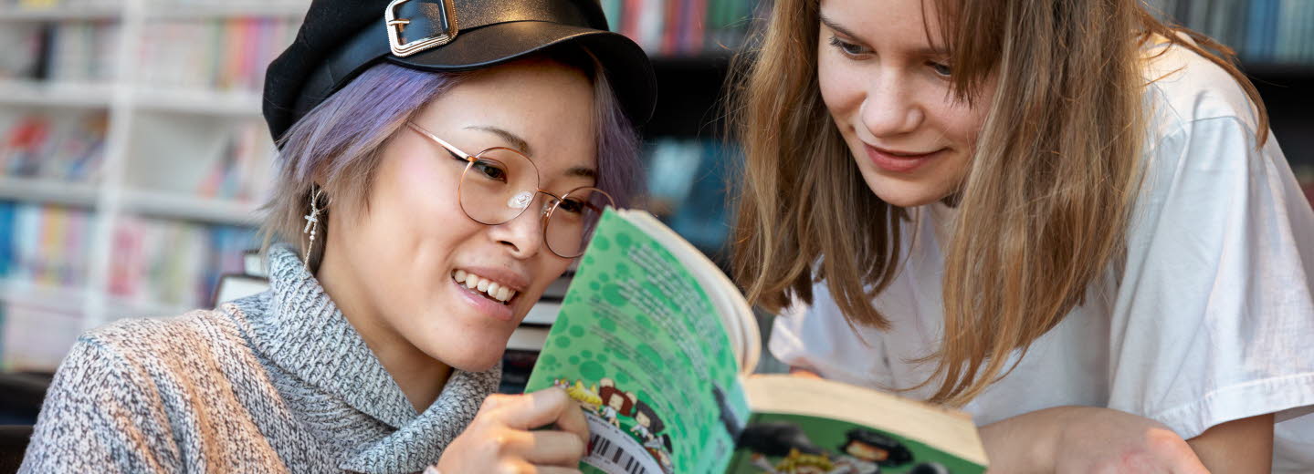 Två ungdomar på ett bibliotek tittar i en bok tillsammans