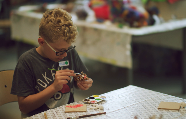 Pojke sitter vid ett bord och målar på figurer.