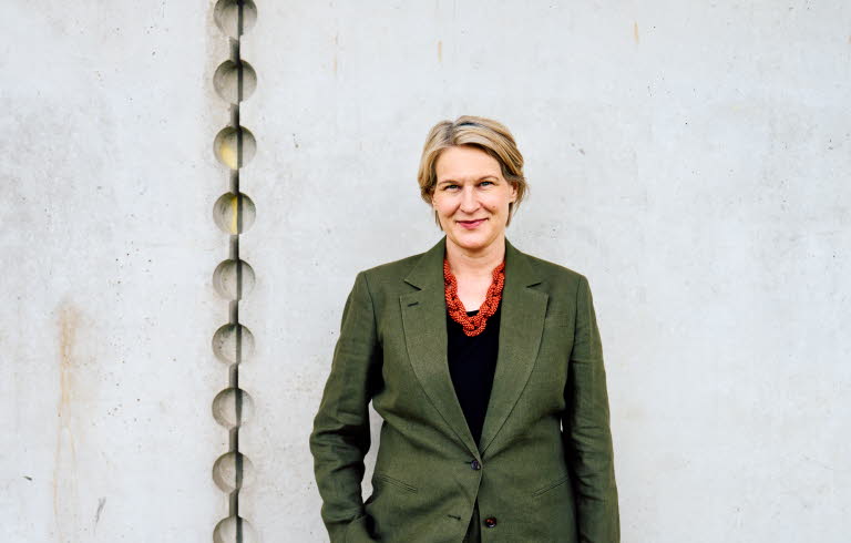 Pressbild på Kajsa Ravin som står framför en grå vägg.