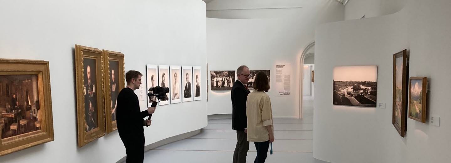Två personer tittar på konst på Östergötlands museum. I bakgrunden står en filmare och filmar.