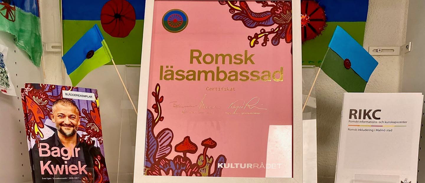 Hylla från bibliotek med intyg på att biblioteket är romsk läsambassad.