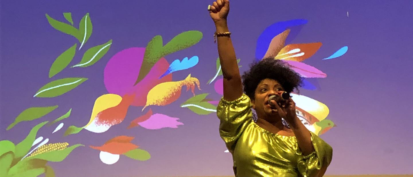 Kvinna som håller en mikrofon i handen och ströcker upp ena handen i luften.