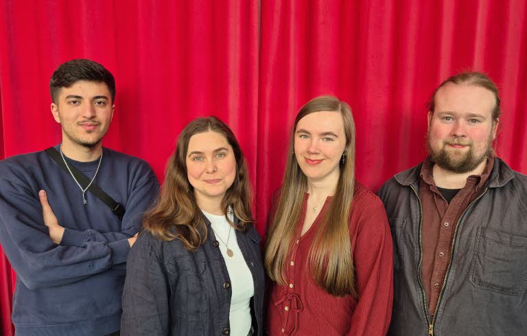 Gruppbild av två kvinnor och två män framför ett rött draperi. 