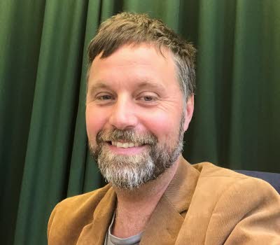 Bild på John Bjerkert, med grön bakgrund.