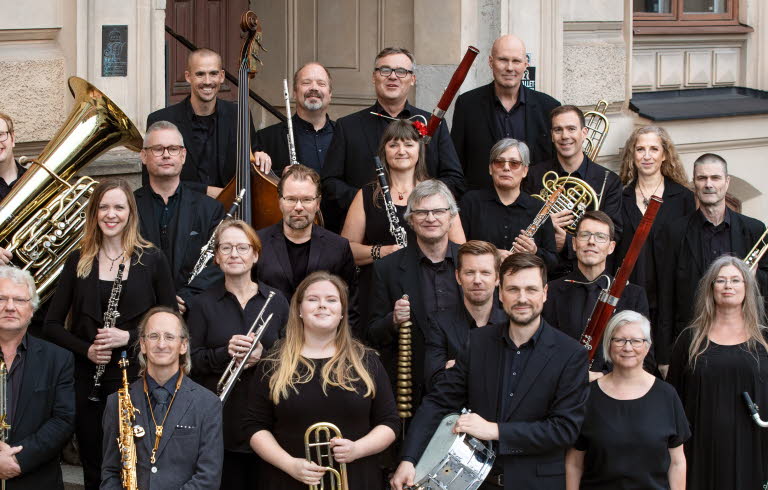 Symfoniorkester står på en trappa, ett tjugotal musiker som håller sina instrument i sina händer.