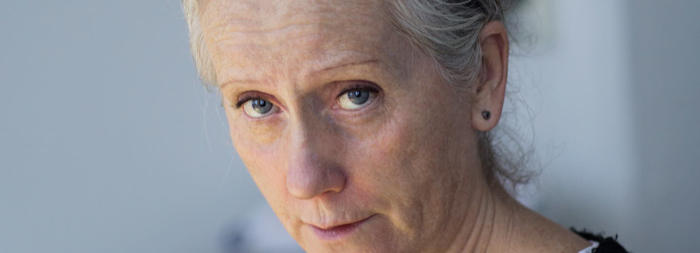 Portrait of Eva Lindström. She's wearing a black sweater and is looking towards the camera, holding a pencil.