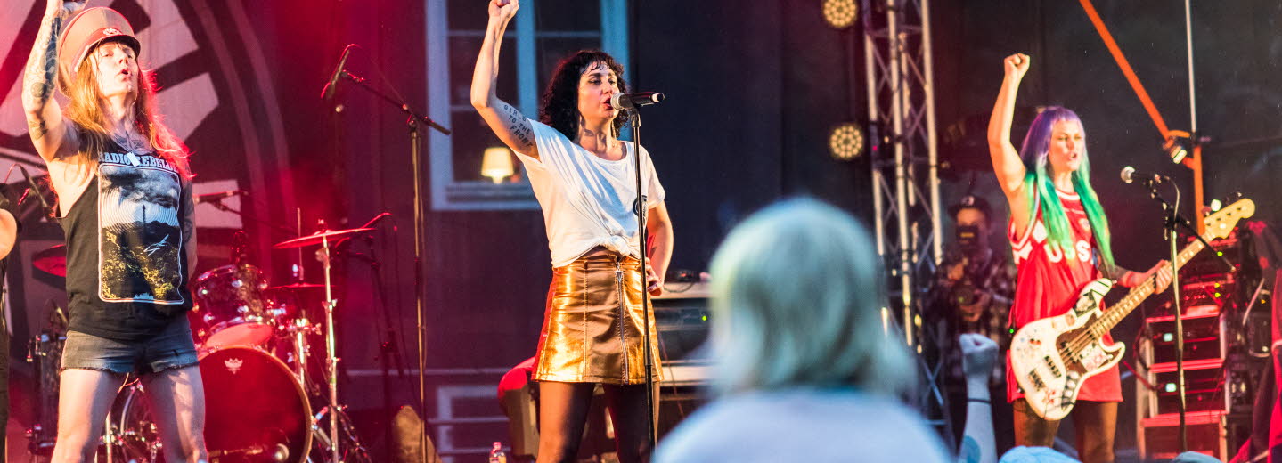 Tre personer som sjunger från en musikscen. Alla tre med uppsträckt högerarm.