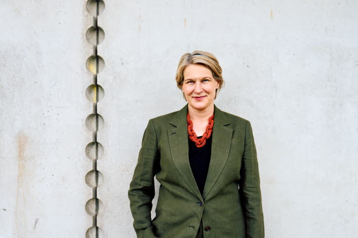 Pressbild på Kajsa Ravin som står framför en grå vägg.