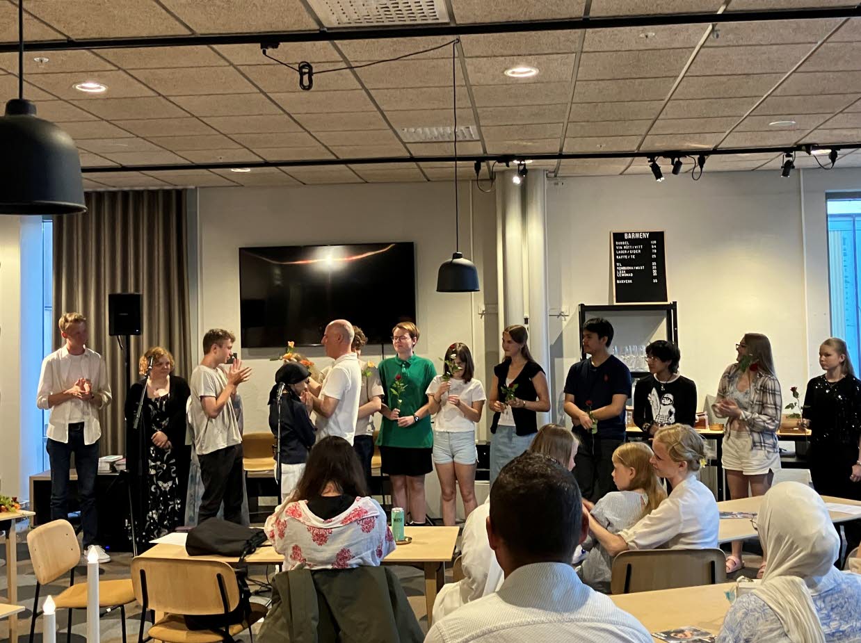 Ungdomar med blommor i händerna står uppradade framför en publik.