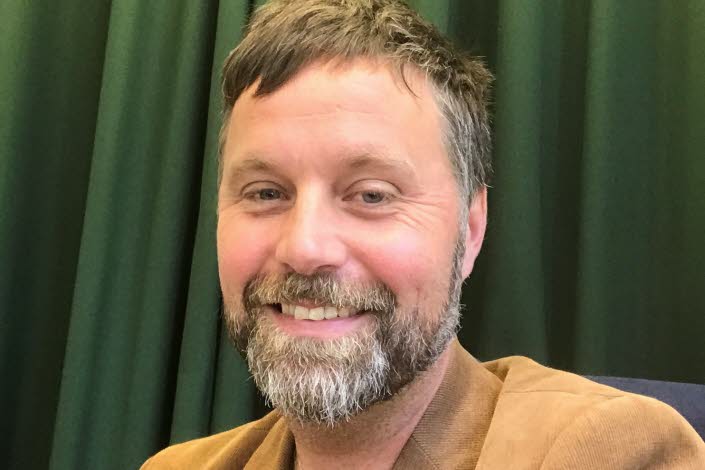 Bild på John Bjerkert, med grön bakgrund.