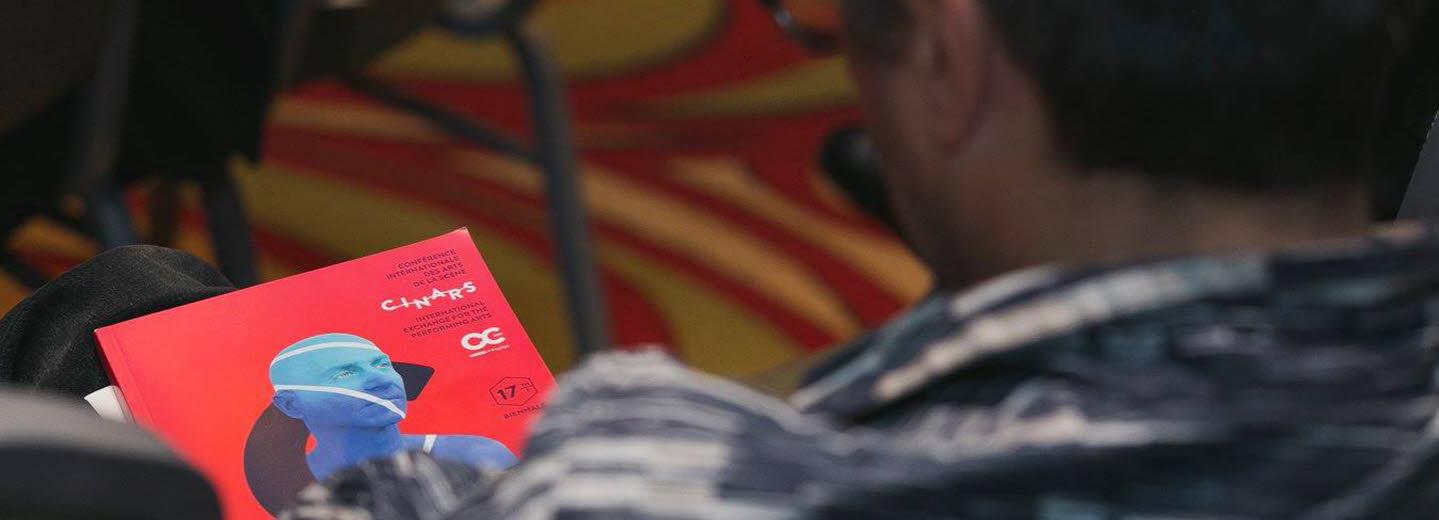 Foto av en man bakifrån som sitter och tittar på programmet för Cinars. Omslaget är rött med en blå man från axlarna och uppåt.