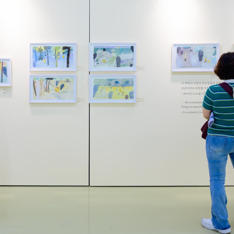 Tre personer tittar på en utställning med teckningar av Eva Lindström under Jeonju internationella bilderboksmässa 2025. Three people are viewing an exhibition of drawings by Eva Lindström at the Jeonju International Picture Book Fair 2025.