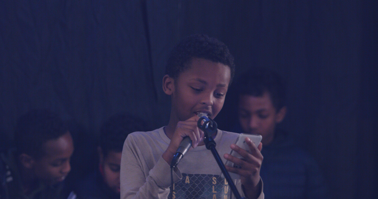 Ett barn som läser från ett papper framför en mikrofon. 