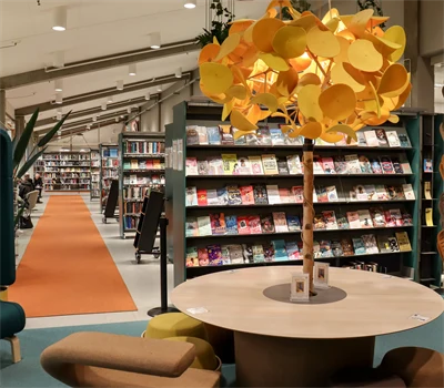 Interiör från bibliotek med bokhyllor, sittmöbler och samlingsbord med en lampa som ser ut som ett träd.