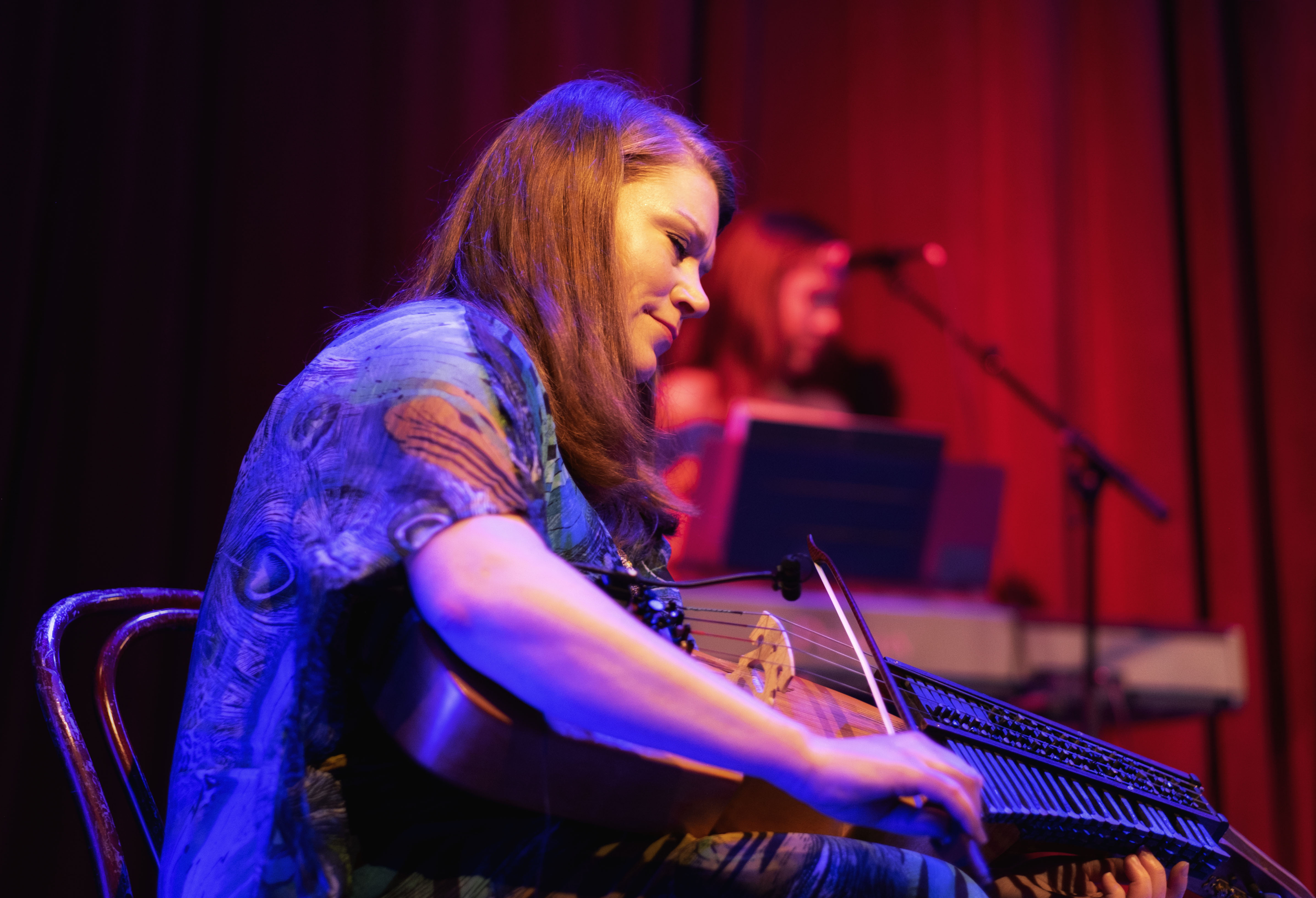 Kvinna spelar nyckelharpa på en scen. I bakgrunden medmusikant på keyboard.